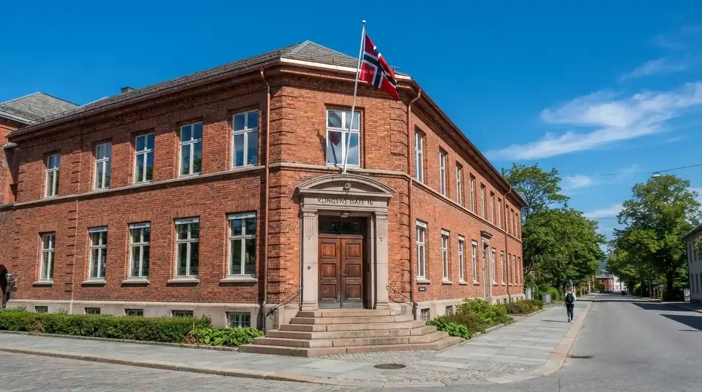 Offentlig kontorbygning i rødt murstein i en norsk by, med et flagg ved inngangen og blå himmel